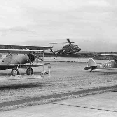 Navy helicopter landing near small planes.