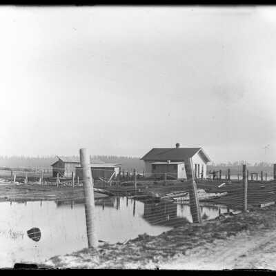 Buildings, pond with logs: Origsize: 4x5; Origformat: Negative