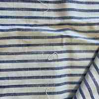 The reverse side of the fabric, showing unpicked threads — Image showing the reverse side of a plain-woven fabric. Navy blue stripes run horizontally along the fabric. Three small pieces of thread are intertwined with the piece, running perpendicular to the stripes.