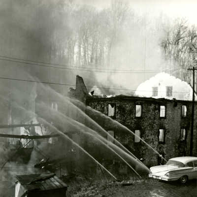 Crowell Tape Mill on fire with firefighters spraying water, 1964
