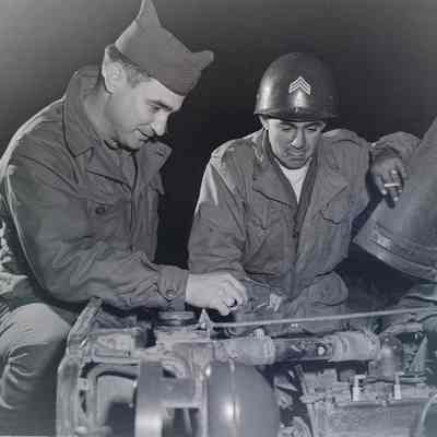 Two soldiers looking under the hood of a Jeep