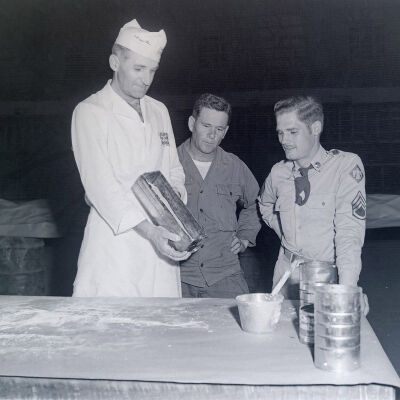 Two soldiers watching a cook prepare bread
