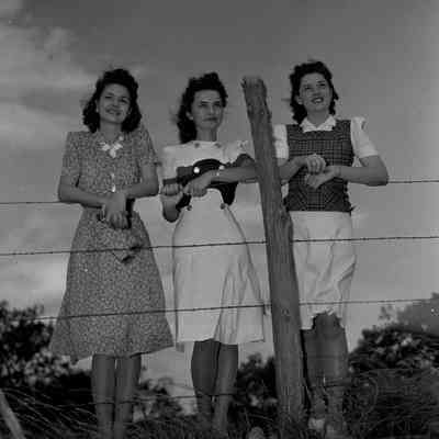 Three girls standing along a barbed wire fence