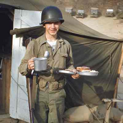 Soldier in front of tent with his mess kit full of food