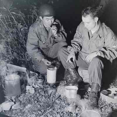 Two soldiers warming C-rations over a campfire