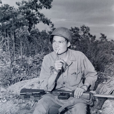 Soldier sitting on a rock smoking a cigarette and holding a BAR