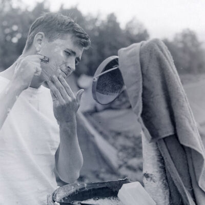 Soldier shaving using his helmet as a water basin