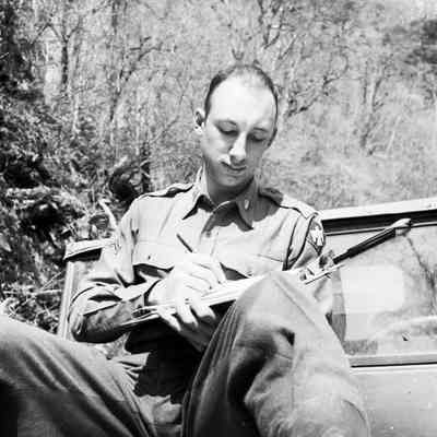 Soldier taking notes on a clipboard while sitting on the hood of a jeep