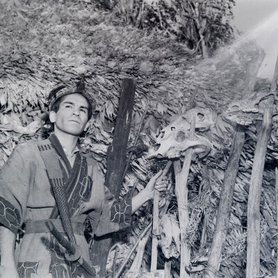 Ainu man in front of a dwelling decorated with animal skulls