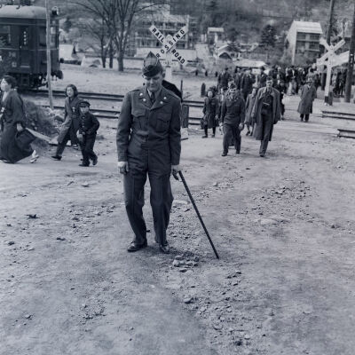 Soldier with cane walking with large group of soldiers and civilians