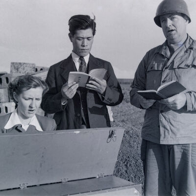 Soldier, Japanese man, and woman singing around a keyboard