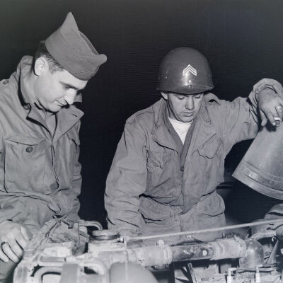 Two soldiers looking under the hood of a Jeep