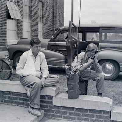 Soldier talking on a field phone next to a man in a sling