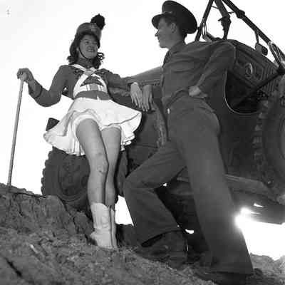 Majorette and soldier posing on the side of a command car