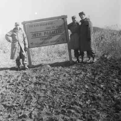 Three soldiers standing around a sign for the 38th Parallel