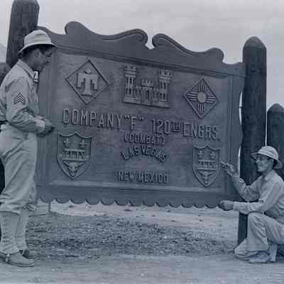 Two soldiers in front of a large carved wood sign
