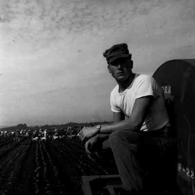 Soldier sitting on a truck with farm workers in the background