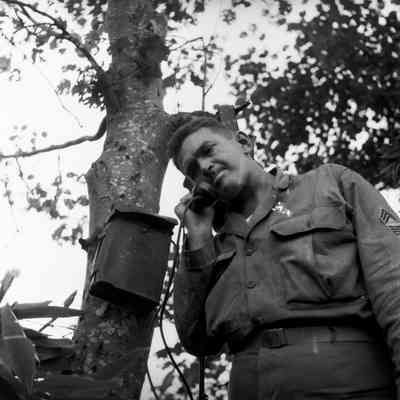 Soldier using a field phone that is strapped to a tree