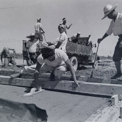 Civilian construction crew pouring concrete and leveling floor for Quonset hut