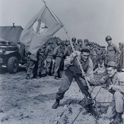 Two soldiers plant the Oklahoma flag in a tent camp