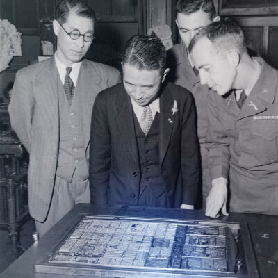 Soldiers and two Japanese civilians examine a printer's type form