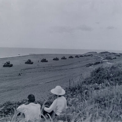 Civilians observing a line of tanks practice-firing out to sea