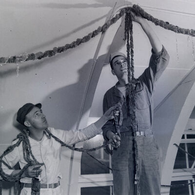 Two soldiers stringing Christmas decorations inside a building