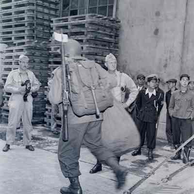 General Styron and Japanese civilians watch as soldiers disembark from a ship