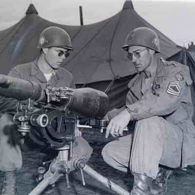 Soldiers examining a recoilless rifle with tent camp in background