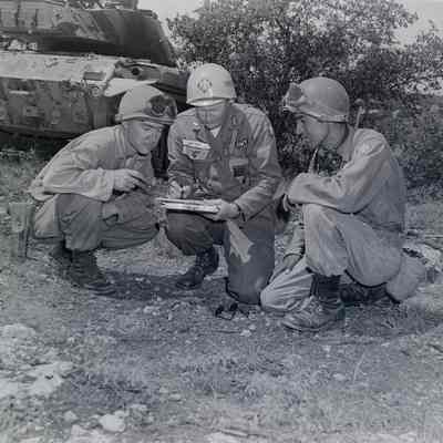 Soldiers examining maps with a tank in the background