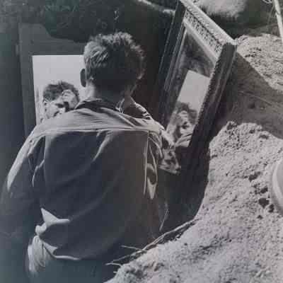 Soldier combing hair with mirror in dugout