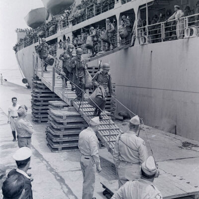 Soldiers with duffel bags and weapons coming down gangway from ship