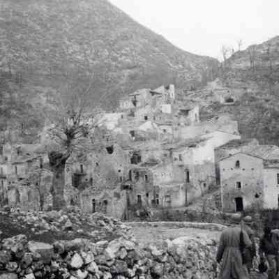 Soldiers march past destroyed homes