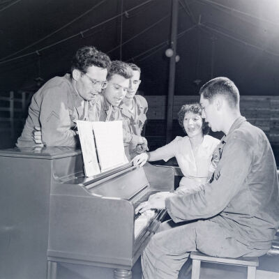 Soldiers and a woman singing around a piano