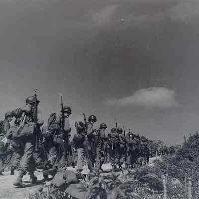 Soldiers marching along a road with weapons slung over their shoulders