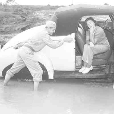Soldier pushing a car out of the mud with a woman sitting in the car
