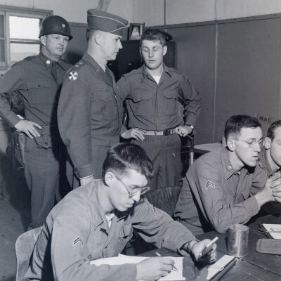 Two-star general talking to officers and enlisted men in an orderly room