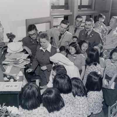Female Army Service Club member, soldiers, children, and a nun singing around a piano