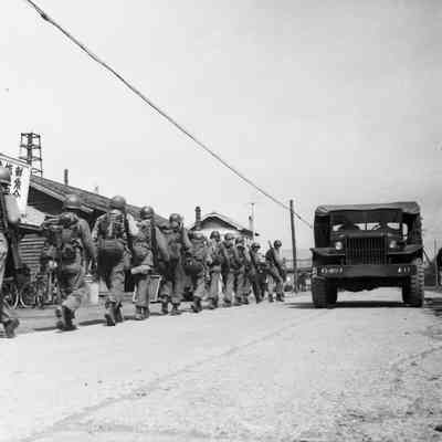Soldiers on a road march through a village