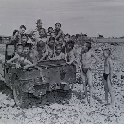 Soldiers in jeep with a large group of Japanese kids