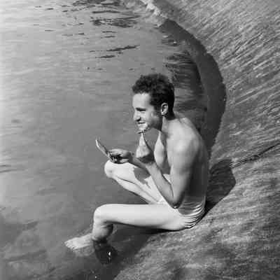 Soldier shaving while sitting at the edge of a lake
