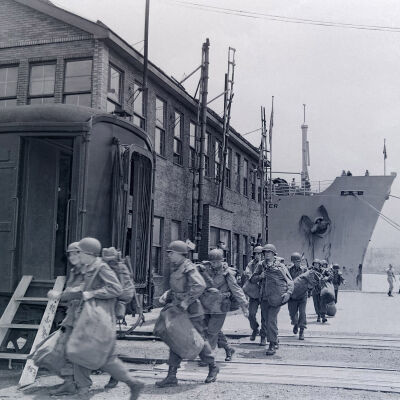 Soldiers with duffel bags and weapons walking through a dock area