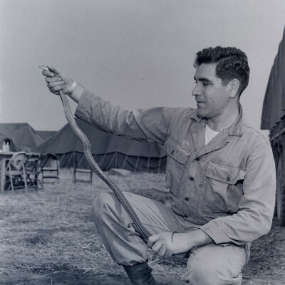 Soldier posing with a snake with a tent camp in background
