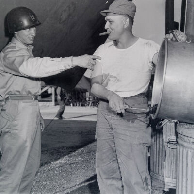 Officer directing a soldier cleaning a pot