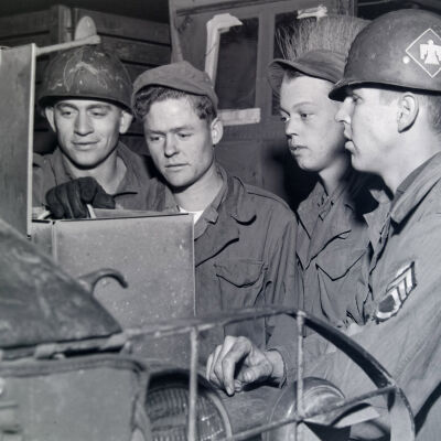 Group of soldiers examining a box on the fender of a truck
