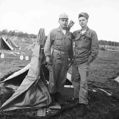 Two soldiers posing in front of tents with cigars