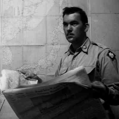 Soldier reading newspaper while standing in front of a wall map