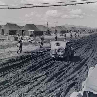 Soldiers and a jeep traveling down a very muddy road through a camp