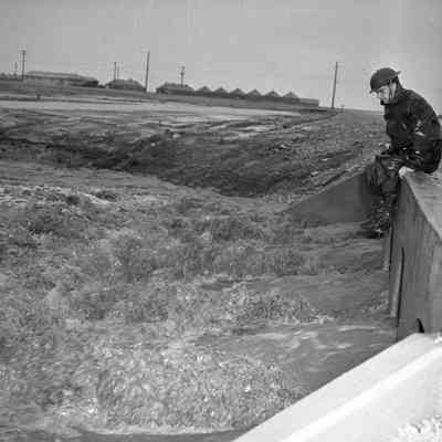 Soldier sitting on a flooding road culvert