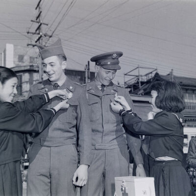 Japanese ladies pinning decorations onto a couple of soldiers